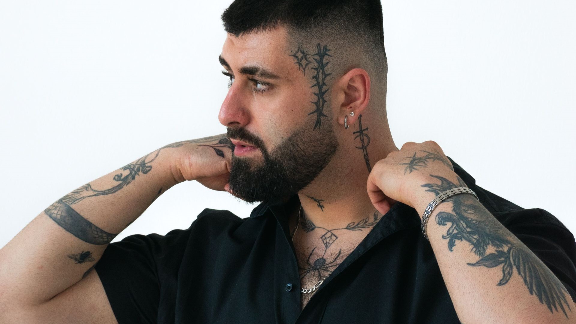 Homem com tatuagens em blackwork nos antebraços e rosto